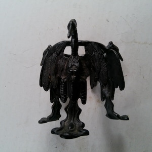 May include: A dark bronze-colored decorative sculpture of a bird with outstretched wings. The bird has detailed feathering and stands on a pedestal base. The sculpture is set against a plain white background.