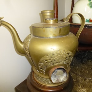 May include: A vintage brass teapot with intricate floral and dragon detailing. The teapot features a curved spout with a dragon head, a handle, and a round base. The brass has a warm, aged patina, suggesting its antique nature.
