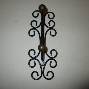 May include: Black metal wall hook with two gold-toned ball finials and a decorative scroll design.