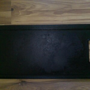 May include: A rectangular, black cast iron griddle with integrated handles. The griddle has a slightly textured surface and is designed for even heat distribution. Ideal for stovetop cooking.