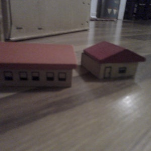 May include: Two miniature houses made of wood. The larger house has a red roof and five windows. The smaller house has a red roof and one window.