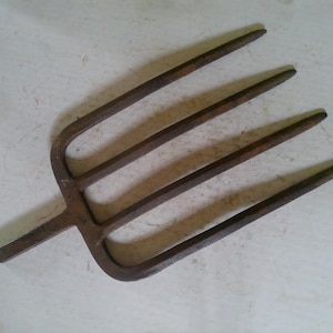 May include: A rusty, four-tined garden fork with a long handle. The tines are evenly spaced and slightly curved, and the handle is attached to the fork's head. The metal has a weathered appearance.