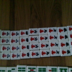 Pu&ograve; includere: Un set di tessere rettangolari da mahjong disposte in file. Le file superiori presentano tessere bianche con caratteri cinesi rossi e neri che rappresentano i numeri da uno a otto. La fila inferiore mostra tessere bianche con motivi circolari verdi.
