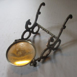 Op de afbeelding: Een gouden metalen standaard met een ronde bovenkant en sierlijke kruldetails. De standaard is ontworpen om een klein object te houden, zoals een fles of een vaas.