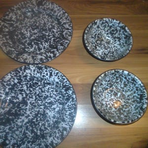 May include: Set of four black and white speckled enamelware plates and bowls. The plates and bowls have a vintage look and are perfect for serving food.