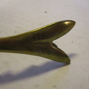 K&ouml;nnte beinhalten: Nahaufnahme eines Vintage-Messingobjekts mit gegabeltem Ende. Das Objekt hat einen warmen, goldenen Farbton und scheint aus massivem Metall zu bestehen. Die Zahlen "149" und die Initialen "BD" sind auf der Oberfl&auml;che eingepr&auml;gt. Der Zweck des Objekts ist unbekannt.