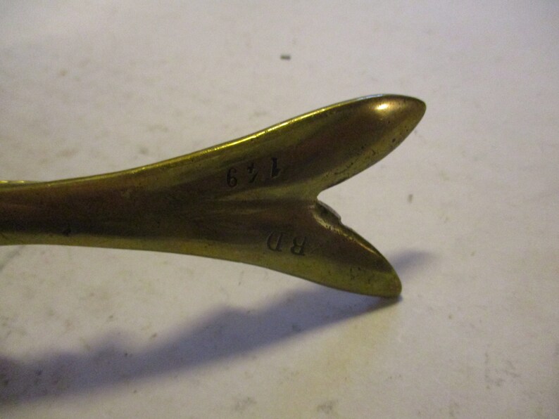 K&ouml;nnte beinhalten: Nahaufnahme eines Vintage-Messingobjekts mit gegabeltem Ende. Das Objekt hat einen warmen, goldenen Farbton und scheint aus massivem Metall zu bestehen. Die Zahlen "149" und die Initialen "BD" sind auf der Oberfl&auml;che eingepr&auml;gt. Der Zweck des Objekts ist unbekannt.