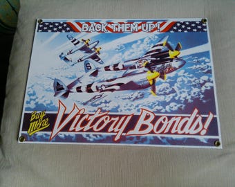 Peut inclure: Panneau métallique vintage représentant deux avions de chasse P-38 Lightning en vol sur fond de ciel bleu nuageux. Le panneau affiche le texte "Back Them Up!" et "Victory Bonds!" en rouge et blanc, sur un thème patriotique.
