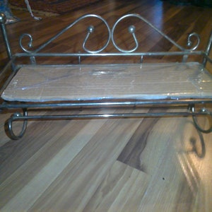 May include: A silver metal shelf with a decorative scroll design and a wooden shelf. The shelf has two hooks on the bottom.