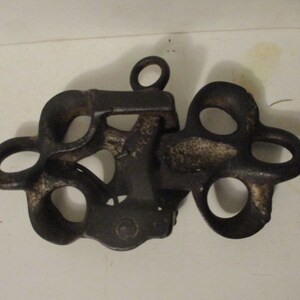 May include: A black cast iron pulley with multiple loops and a single ring at the top.