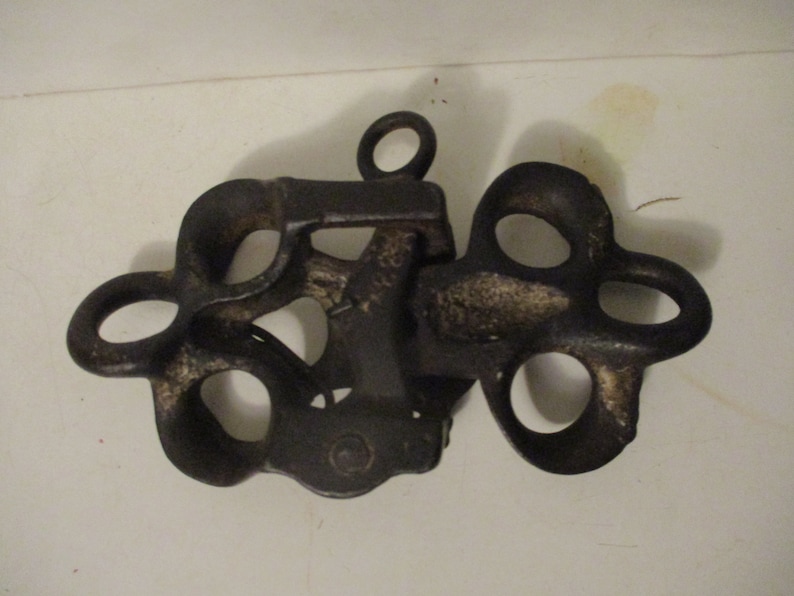 May include: A black cast iron pulley with multiple loops and a single ring at the top.