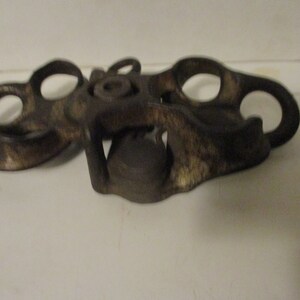 May include: A vintage metal bottle opener with a unique design. The opener has two loops on each side and a central mechanism for opening bottles.