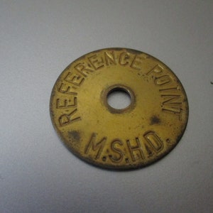 May include: A round, brass-colored metal tag with the words "REFERENCE POINT" and "M.S.H.D." embossed around a central hole. The tag has a worn, aged appearance.