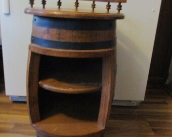 May include: A wooden barrel-shaped side table with a small shelf and a decorative top rail. The table is made of brown wood with black accents and has a rustic, vintage appearance. The table is approximately 30 inches tall.
