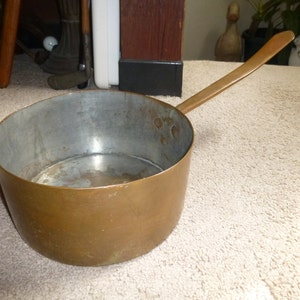 May include: A vintage copper saucepan with a long handle. The saucepan has a shiny copper exterior and a silver interior.