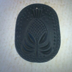 May include: A black cast iron mold shaped like a pineapple with a detailed design. The mold is used for baking or making decorative items.