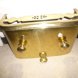 May include: A vintage brass bathtub with decorative handles and a floral design on the top edge. The tub has a polished finish and is designed to be mounted on a wall. The overall dimensions are approximately 30 inches wide.