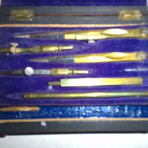 May include: A wooden box with a purple velvet interior containing a set of six antique brass compasses. The compasses are arranged in rows and are all closed.
