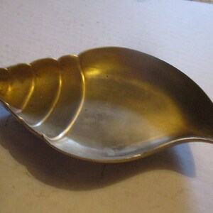 May include: A gold-colored metal seashell-shaped dish. The dish is smooth and has a slightly curved shape.