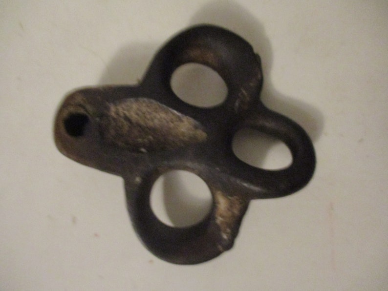 May include: A dark gray metal hook with three holes. The hook is shaped like a clover leaf.