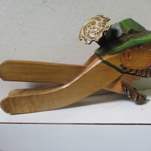 May include: A wooden nutcracker in the shape of a man wearing a green hat with a brown and white feather. The nutcracker is painted with details on the face and beard.