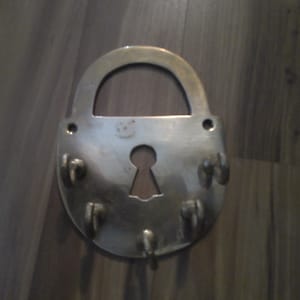 May include: A silver metal key holder shaped like a padlock with six hooks. The key holder is a decorative piece for the home.