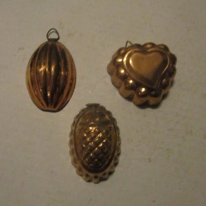 May include: Three vintage copper cake molds. One is shaped like a heart, one is oval with a ribbed design, and the other is oval with a textured design.