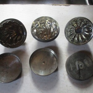 May include: Six vintage metal cake molds with different designs. The molds are round and have a smooth, silver finish. Some of the molds have a floral design, while others have a more abstract design.