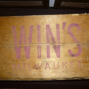 May include: A wooden crate with metal banding and the words "WIN'S MILWAUKEE" printed in pink.