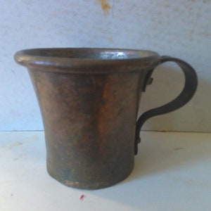 May include: A copper mug with a dark brown handle. The mug has a slightly flared lip and a rounded bottom.