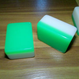 Pu&ograve; includere: Due tessere rettangolari da Mahjong con una finitura liscia e lucida. Una tessera &egrave; posizionata verticalmente mostrando una parte superiore verde brillante e una base bianca, mentre l'altra &egrave; inclinata per rivelare la parte superiore bianca e la base verde. &Egrave; visibile una terza tessera con il disegno di un uccello rosso.