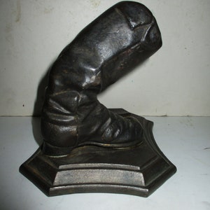 May include: A cast iron boot bookend in black. The boot is bent at the ankle and is on a square base.