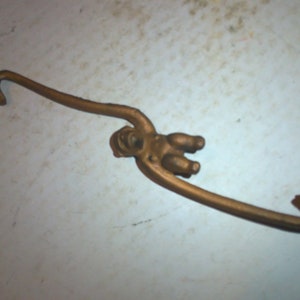 May include: A gold-colored metal monkey figurine with a long tail that is bent into a hook shape. The monkey is hanging from the hook.