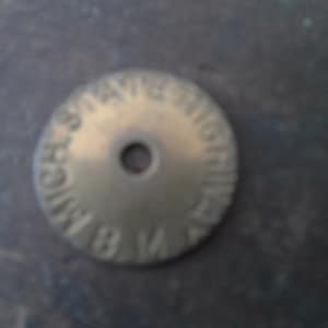 May include: A brass round disc with the words "Bay State Highway" engraved around the edge. The disc has a hole in the center.