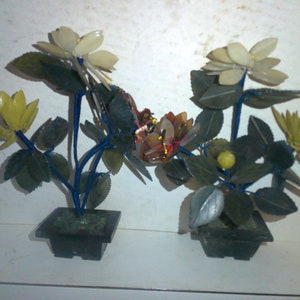 May include: Two jade flower arrangements in black pots. The flowers are made of jade and are in shades of green, white, and yellow. The stems are wrapped in blue wire.