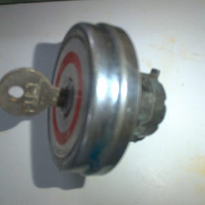 May include: A silver gas cap with a key attached. The gas cap has a red and white circle design.