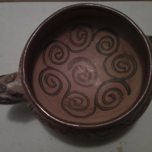 May include: A brown ceramic bowl with a handle shaped like a stylized animal head. The bowl is decorated with a black and brown swirl pattern.