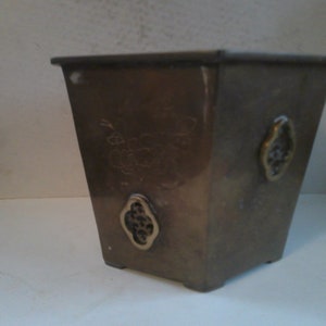 May include: A square brass planter with intricate floral designs etched into the surface. The planter has four decorative accents on the sides.