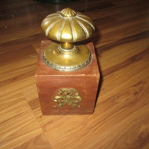 May include: A wooden doorstop with a brass knob on top. The doorstop has a decorative brass design on the front.