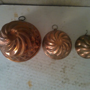 May include: Three copper cake molds with a swirl design. The molds are different sizes and have a shiny finish.