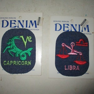 May include: Two iron-on denim patches featuring astrological signs. The left patch is blue with a green Capricorn symbol and the text "Capricorn". The right patch is blue with a pink Libra symbol and the text "Libra".