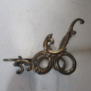 Op de afbeelding: Een gouden metalen decoratieve standaard met een zwierig ontwerp. De standaard heeft een ronde bovenkant en drie poten.