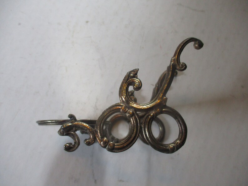 Op de afbeelding: Een gouden metalen decoratieve standaard met een zwierig ontwerp. De standaard heeft een ronde bovenkant en drie poten.