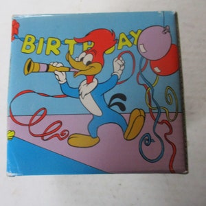 Puede incluir: Un p&aacute;jaro carpintero de dibujos animados azul y rojo con un sombrero rojo sopla un cuerno de fiesta. El fondo es azul con una franja rosa y morada. Las palabras "Birthday" est&aacute;n escritas en letras amarillas. Hay serpentinas rojas, amarillas y azules y globos morados y rojos.