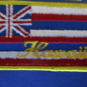 May include: A yellow embroidered patch with the Hawaiian flag and the word "Hawaii" in gold lettering.