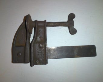 May include: A rusty metal clamp with a wing nut and a long metal bar. The clamp has the number "804" and a logo printed on it.