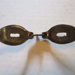 May include: A vintage brass nutcracker with a detailed design. The nutcracker has an oval-shaped head with a rectangular opening and a textured interior. The handles are ribbed. The nutcracker is a kitchen tool.