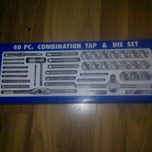 May include: A blue metal case containing a 40-piece combination tap and die set. The set includes various taps, dies, and tools for threading and cutting. The text "40 PC. COMBINATION TAP & DIE SET" is printed on the case.