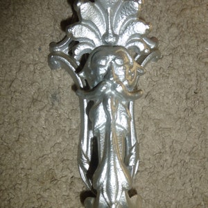 May include: Silver metal wall hook with a decorative design featuring a stylized face with a beard and a floral motif.