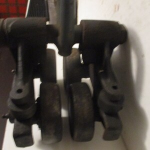 May include: A close-up of a vintage, dark gray metal tool. The tool has a handle and several rounded components, including what appear to be wheels. The object is set against a white surface.